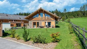 A large wooden lodge with a balcony, stone walls, and a well-maintained lawn.