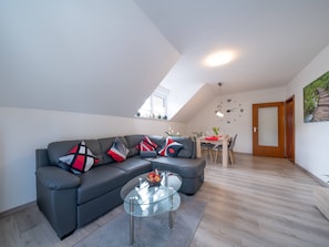 Una sala moderna con un sofá modular, una mesa de centro de vidrio, una zona de comedor con mesa de madera y un reloj en la pared.