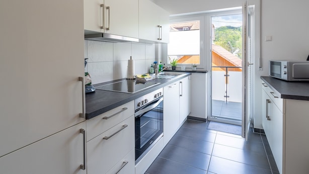 Une cuisine moderne avec des armoires blanches, une hotte de cuisinière en acier inoxydable et un plan de travail noir.