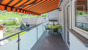 Un balcon avec une table et des chaises, une vue sur les environs et une partie abritée avec des auvents orange.