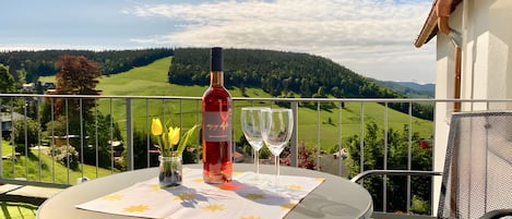 A table with a bottle and glasses on a balcony overlooking a green landscape.
