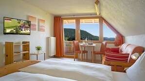 A bedroom with a bed, a desk, a chair, a TV, and a window with a view.