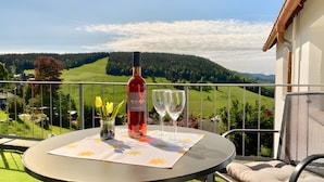 Una mesa con una botella y copas en un balcón con vistas a un paisaje verde.