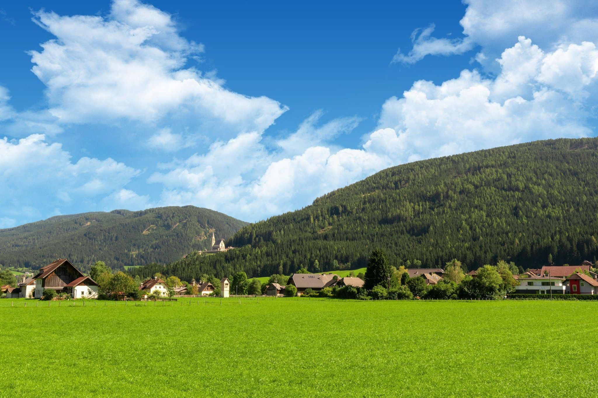 A rural landscape with a church, houses, and a green field.
