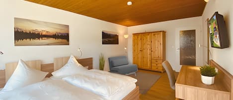 A bedroom with a bed, a desk, a chair, a wardrobe, and two wall-mounted paintings.