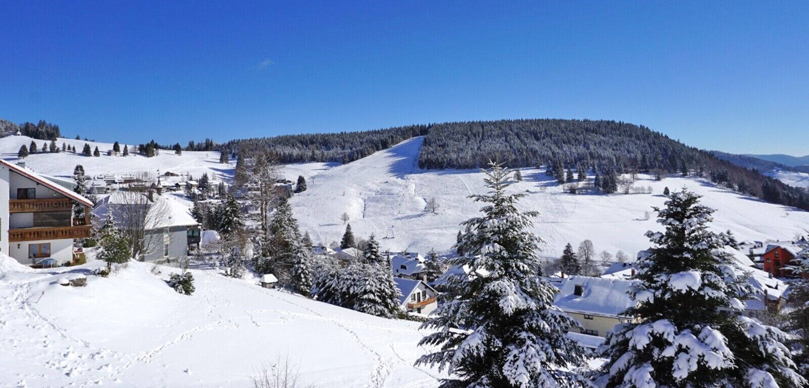 A snow-covered landscape with a building featuring a sloped roof and a visible balcony.
