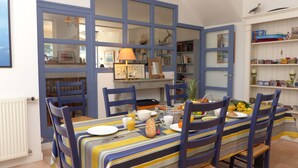 A dining area with a table set for breakfast, chairs, a bookshelf, and a window with a view. - Croix du Sud - cosy town centre house (La Trinité-sur-Mer)