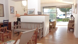 A cozy living room with wooden furniture, a sofa, and a dining table. There is a window with a view of the outside. - Croix du Sud - cosy town centre house (La Trinité-sur-Mer)