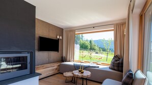 A modern living room with a fireplace, a large window with a scenic view, a sofa, and a small round table with candles.