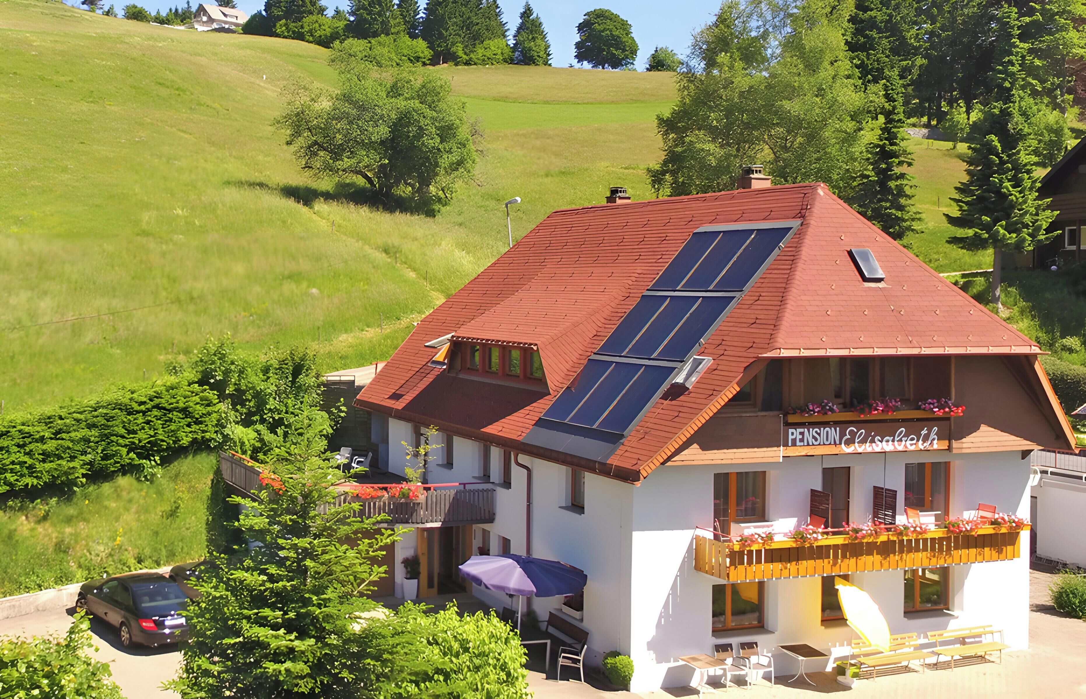 Ein Gebäude mit rotem Dach, Solaranlagen und einem Schild mit der Aufschrift 'Pension Elisabeth'.