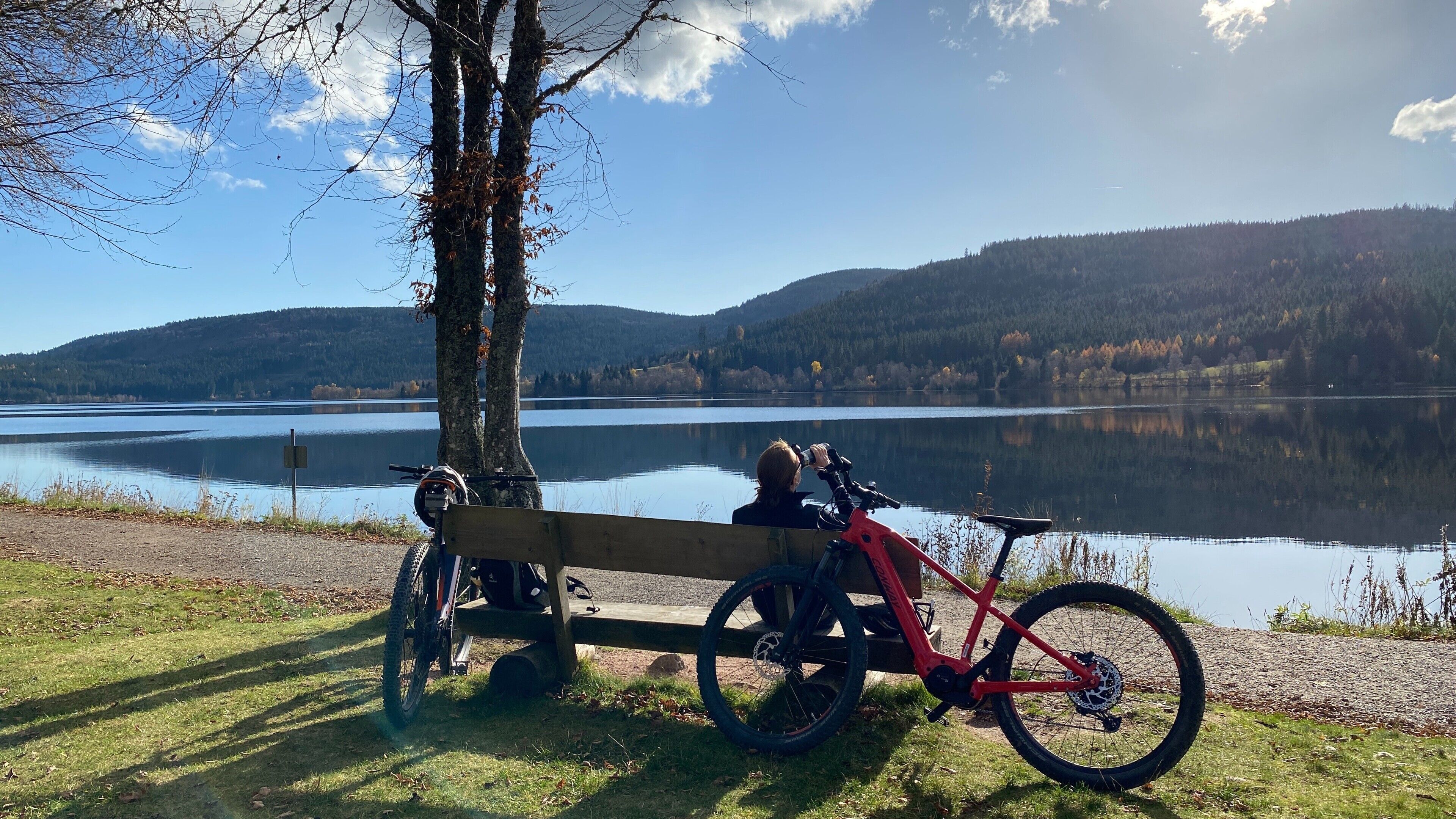 A bench by a lake with a bicycle and helmet.