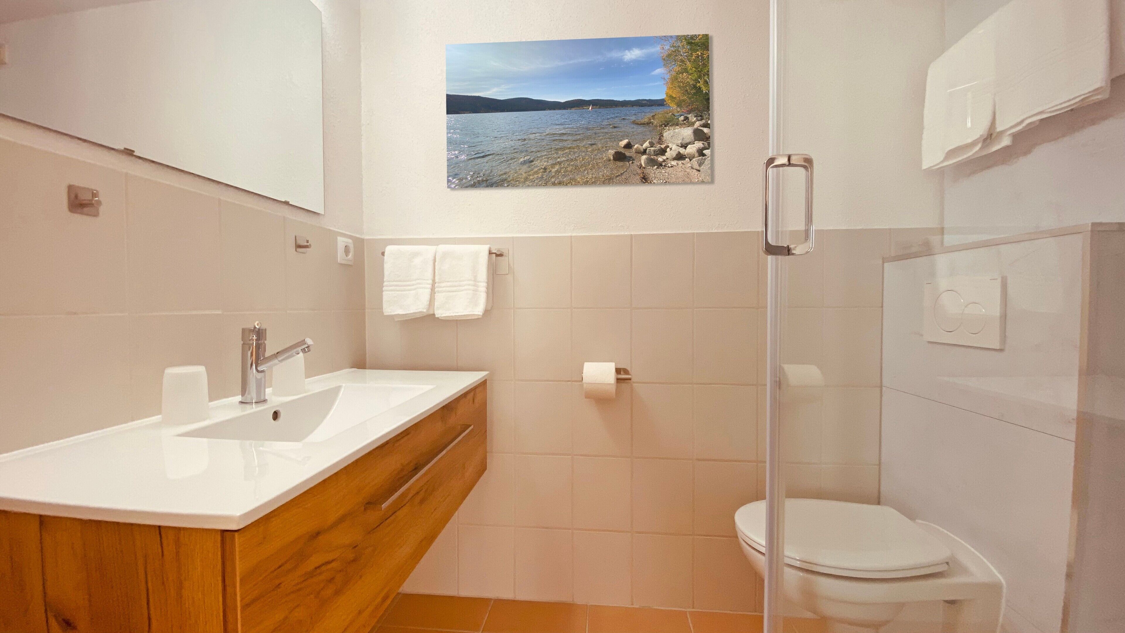 Une salle de bain avec un meuble-lavabo en bois, un lavabo blanc, des toilettes et une cabine de douche en verre.