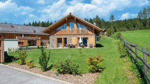 A large wooden house with a balcony, stone walls, and a well-maintained lawn.