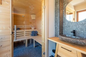 Uma sala de sauna com bancos de madeira, um banco com toalhas, uma pia de pedra e um espelho.