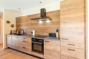 A modern kitchen with wooden cabinetry, a built-in oven, and a stainless steel range hood.