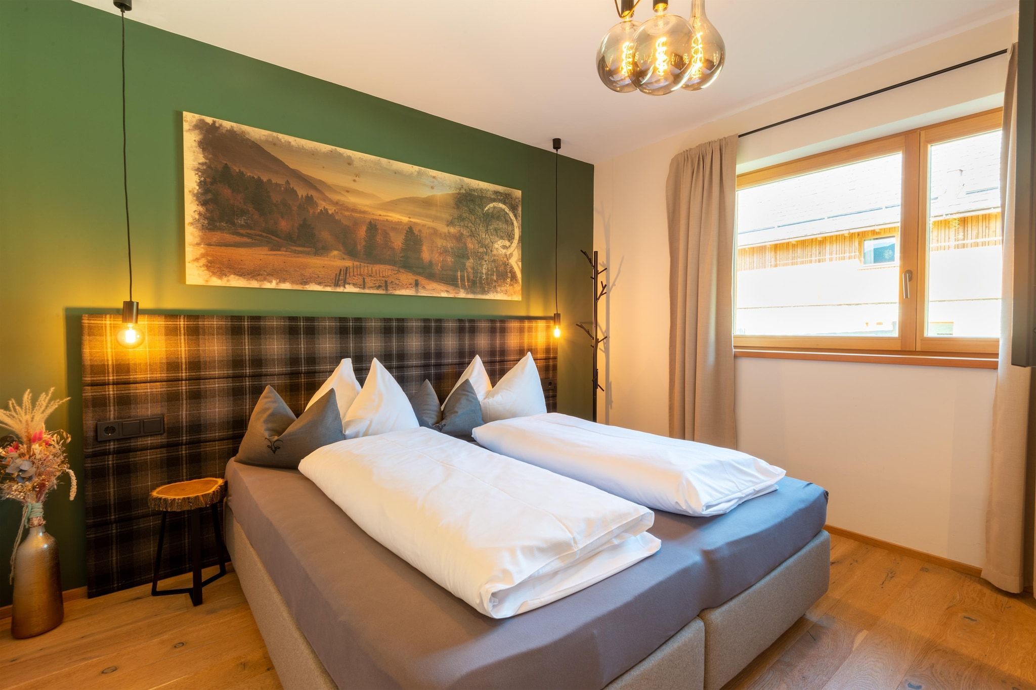 Un lit double bien fait, avec du linge de lit blanc, une tête de lit à carreaux et un grand tableau représentant un paysage, accroché au-dessus.