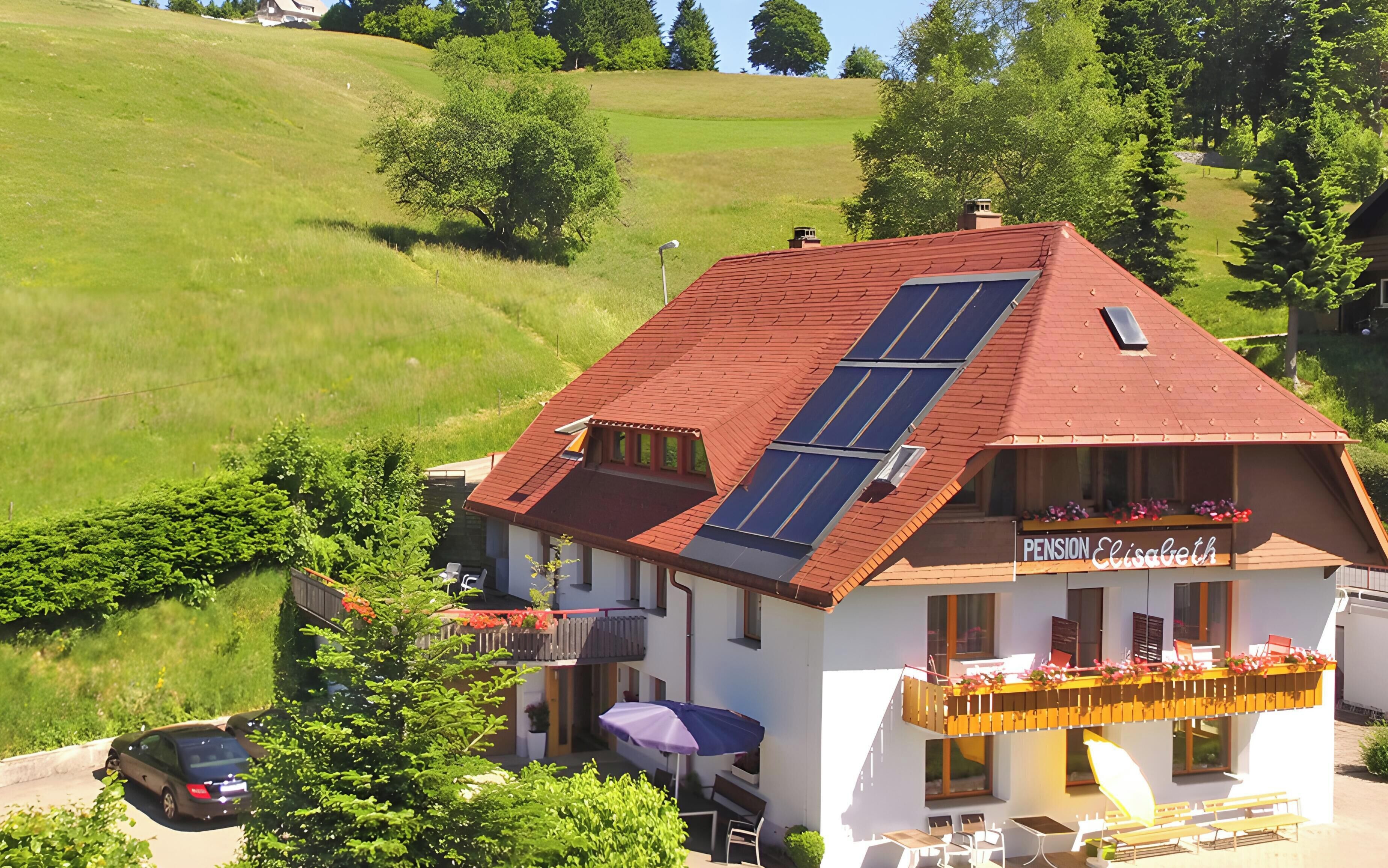 Ein Gebäude mit rotem Dach, Solaranlagen und einem Schild mit der Aufschrift 'Pension Elisabeth'.