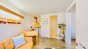 Ein Wohnzimmer mit einer Couch, einem Esstisch und einer Küche im Hintergrund.