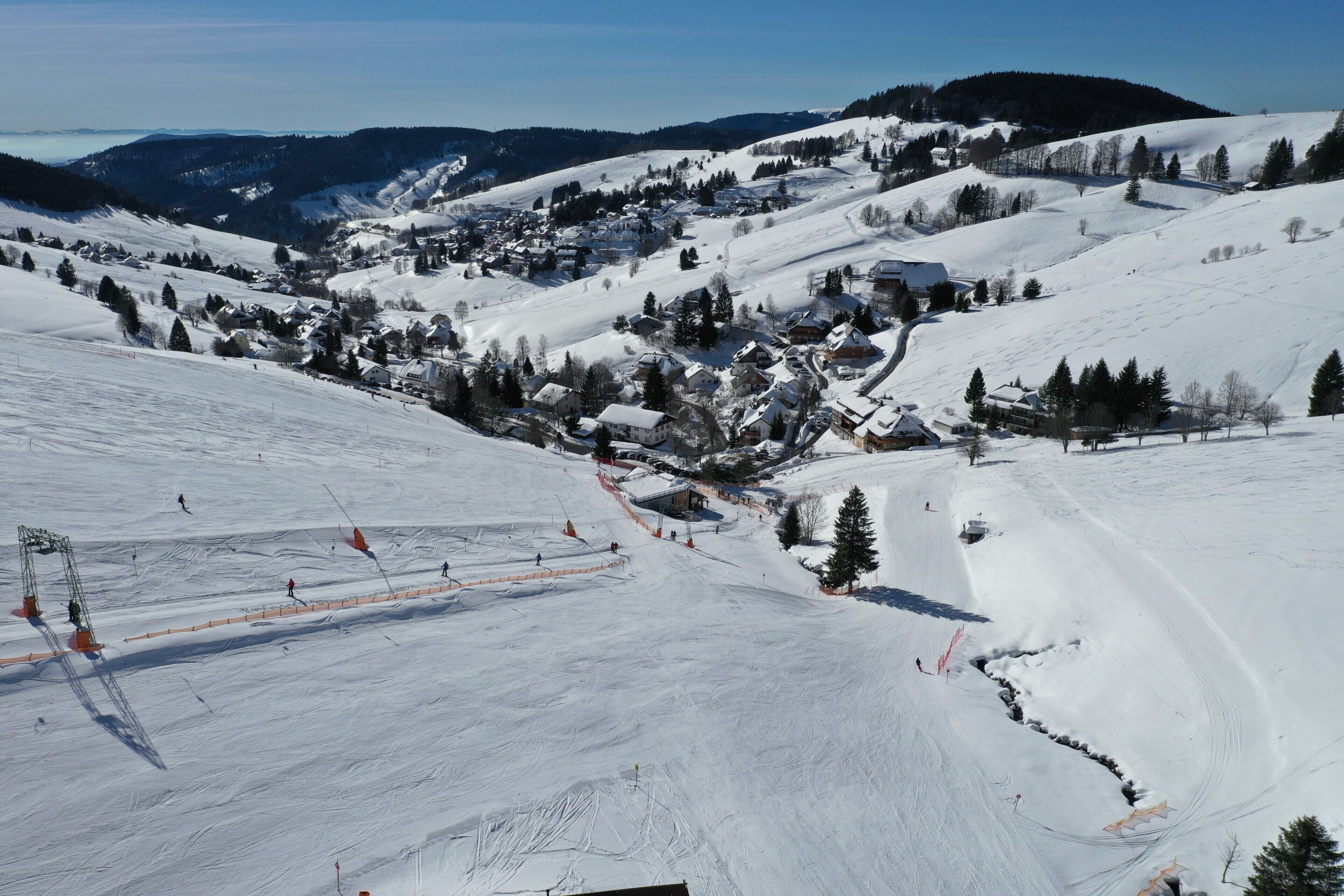 Une station de ski enneigée avec des pistes, une ville avec des bâtiments et une montagne en toile de fond.