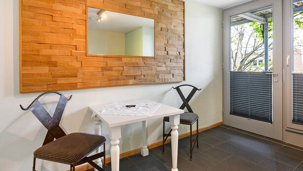 Une pièce avec un mur recouvert de lambris en bois, une table blanche, deux chaises et une porte avec des stores.