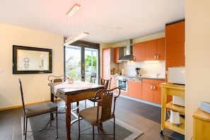 Une cuisine moderne avec des meubles de couleur orange, une table à manger avec des chaises et une vue sur l’extérieur.