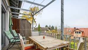 Une terrasse en bois avec une table et des chaises, une clôture en bois et, en arrière-plan, une vue sur des maisons.