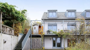 Une maison à deux étages avec un escalier, une porte en bois et une allée pavée.