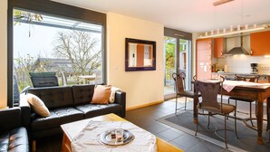 Un salon moderne comprenant un canapé, une table à manger et des chaises, une cuisine équipée et de grandes fenêtres.