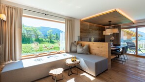 A modern living room with a sofa, a small round table, and a view of a mountainous landscape through large windows.