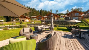 A wooden deck with outdoor furniture, a pond, and a stone wall.