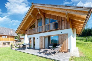 Eine Holzchalet mit Balkon, Sitzgelegenheit im Freien und großen Fenstern.