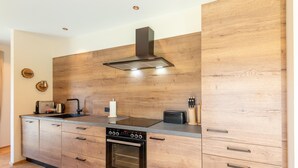 A modern kitchen with wooden cabinetry, a built-in oven, and a stainless steel range hood. - Chalet in Wölting with natural swimming pond (Wölting)