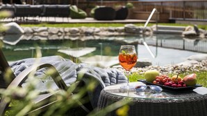A poolside setting with a glass table featuring a drink, fruit, and sunglasses.