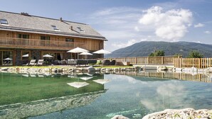 A wooden building with a pool, outdoor seating, and a mountain view.