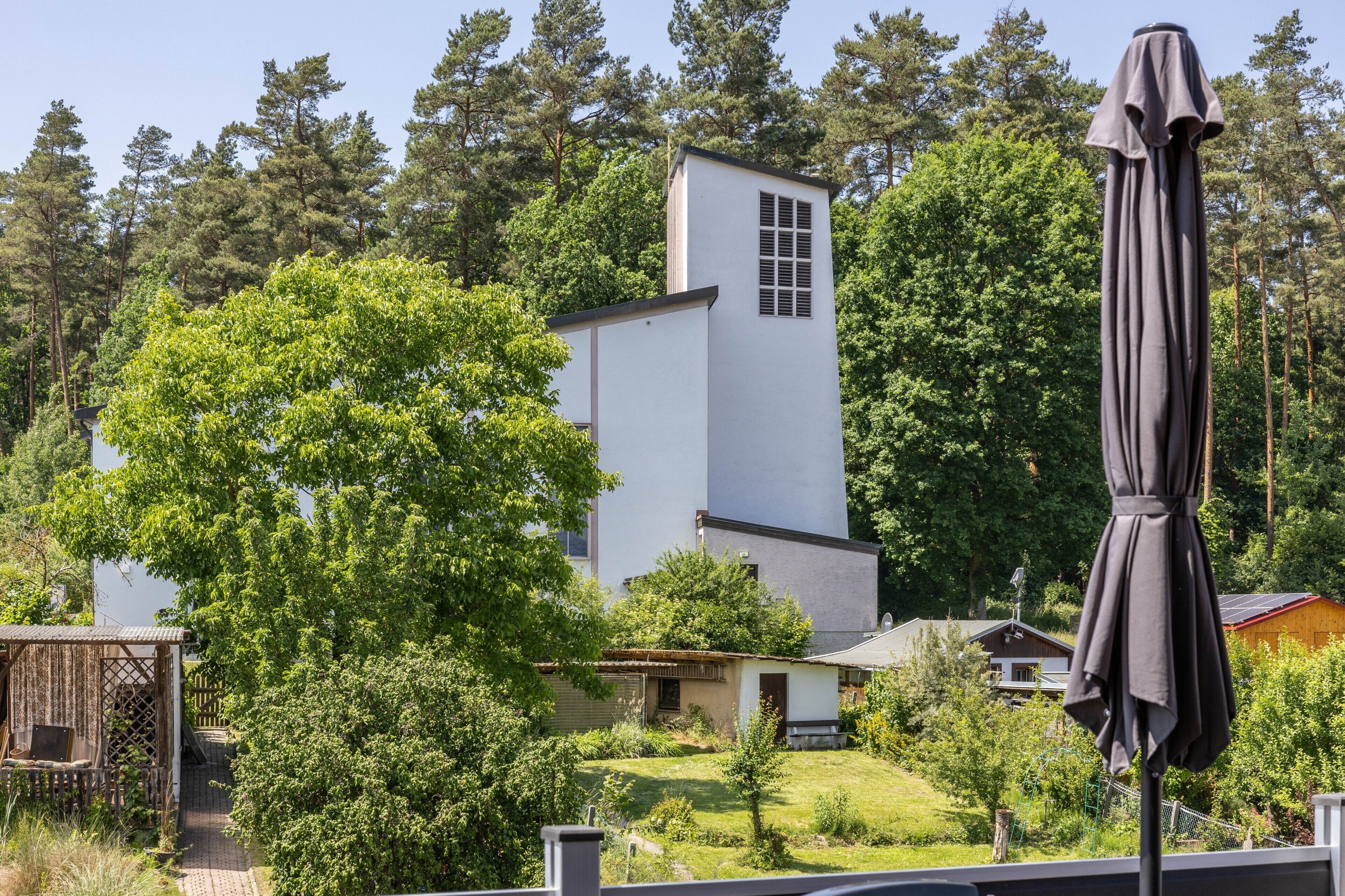 Un bâtiment blanc avec une petite tour, entouré d’arbres et d’un jardin.
