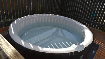 A hot tub with a control panel, surrounded by a wooden fence and a brick floor.