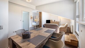 A modern interior with a wooden dining table, cushioned chairs, a sofa, and a television in a corner.