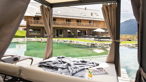 A room with a view of a pool and a wooden building. - Chalet in Wölting with natural swimming pond (Wölting)