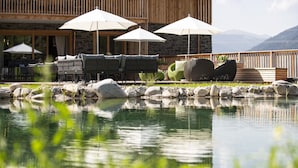 An outdoor seating area with umbrellas, a stone building, and a pond. - Chalet in Wölting with natural swimming pond (Wölting)