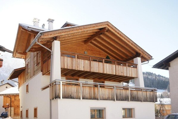 A multi-story building with a wooden balcony and a white facade.