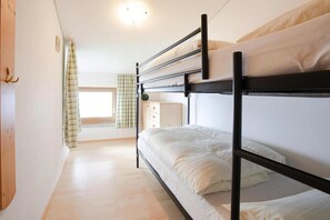 A bunk bed room with a wooden floor, a small dresser, and a window with curtains.