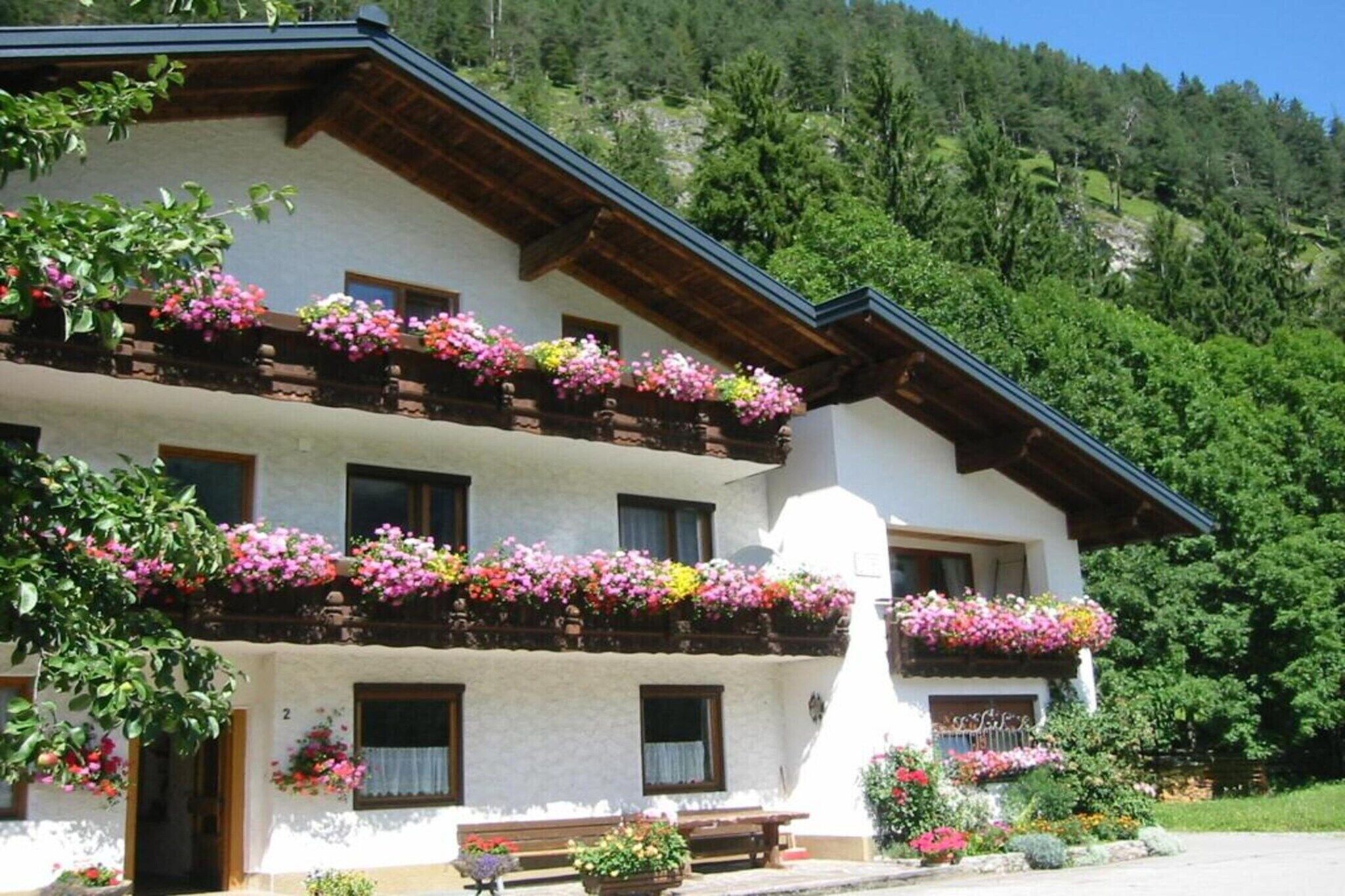 Ein traditionelles Chalet mit Balkonen, die mit bunten Blumen geschmückt sind, vor einer Bergkulisse.