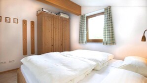 Een slaapkamer met een houten garderobe, een raam met ruitgordijnen en een bed met witte beddengoed.