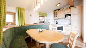 Een gezellige keuken met een groen gestoffeerde bank, een houten eettafel en witte kasten.