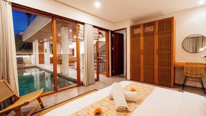 A modern hotel room with a large sliding glass door leading to a pool area, a wooden desk, a chair, and a bed with towels. - Villa Casanaya Pererenan Canggu (Canggu)