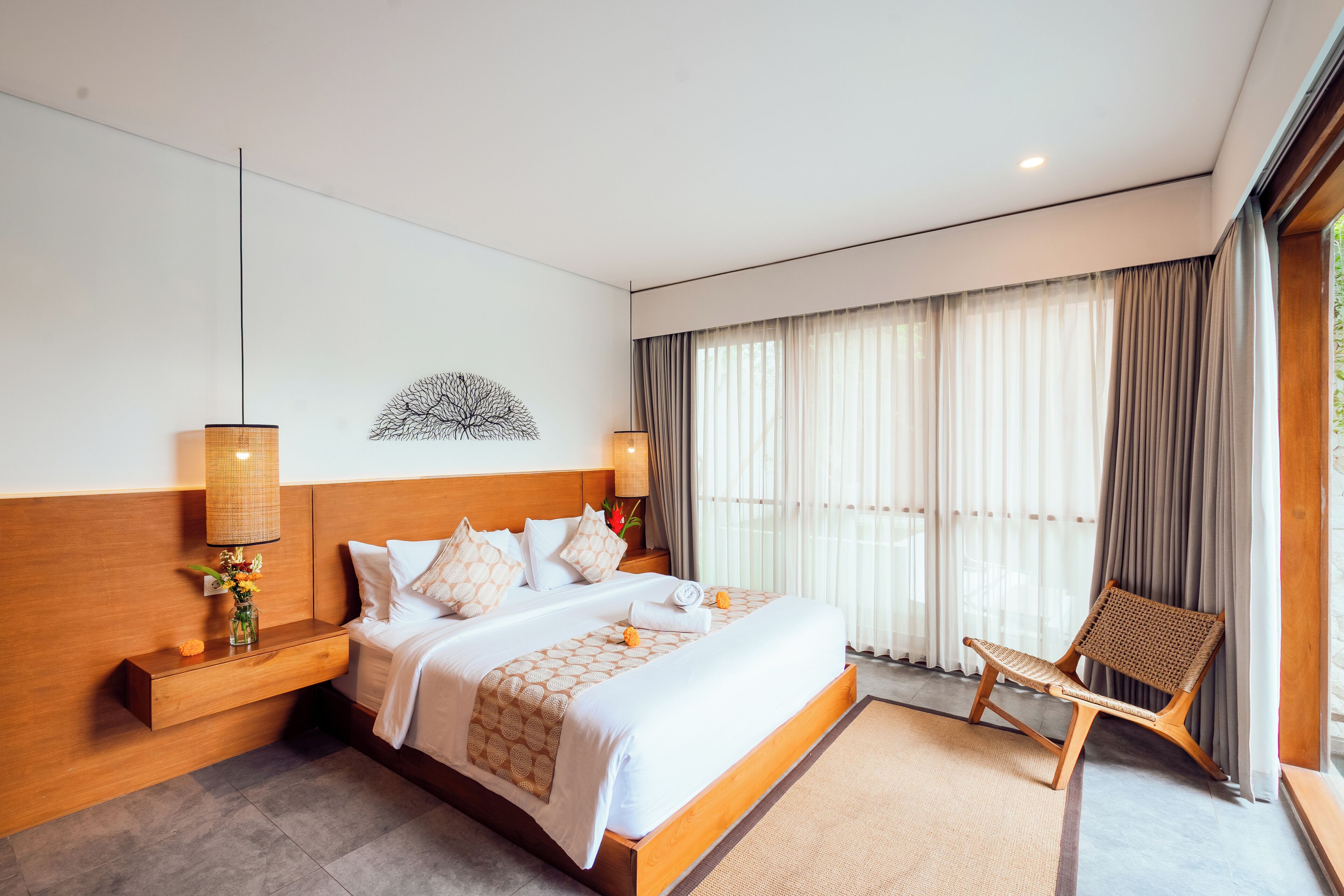 A modern hotel room with a large bed, a wooden nightstand, a wall-mounted lamp, and a window with curtains.