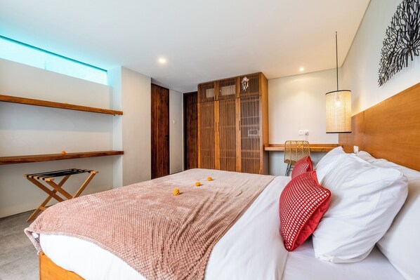 A modern bedroom with a wooden bed, a red and white pillow, a wooden headboard, a wall-mounted light fixture, and a wooden shelf. - Villa Casanaya Pererenan Canggu (Canggu)