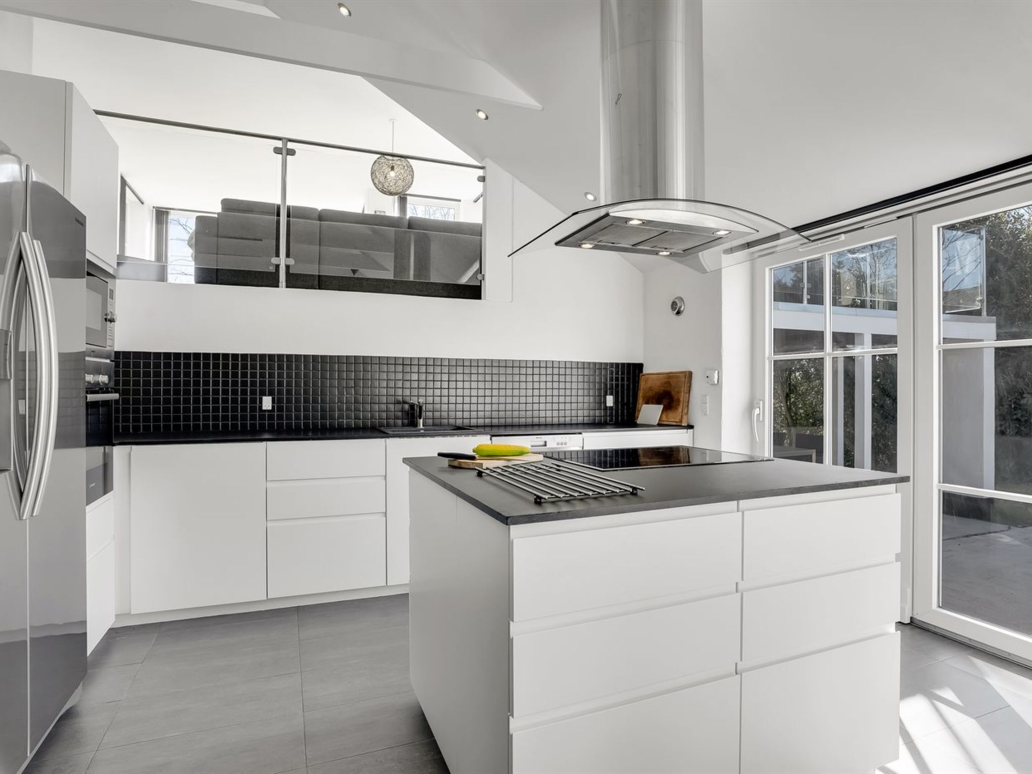 A modern kitchen with a central island, black tiled backsplash, and a large window providing a view of the outdoors.