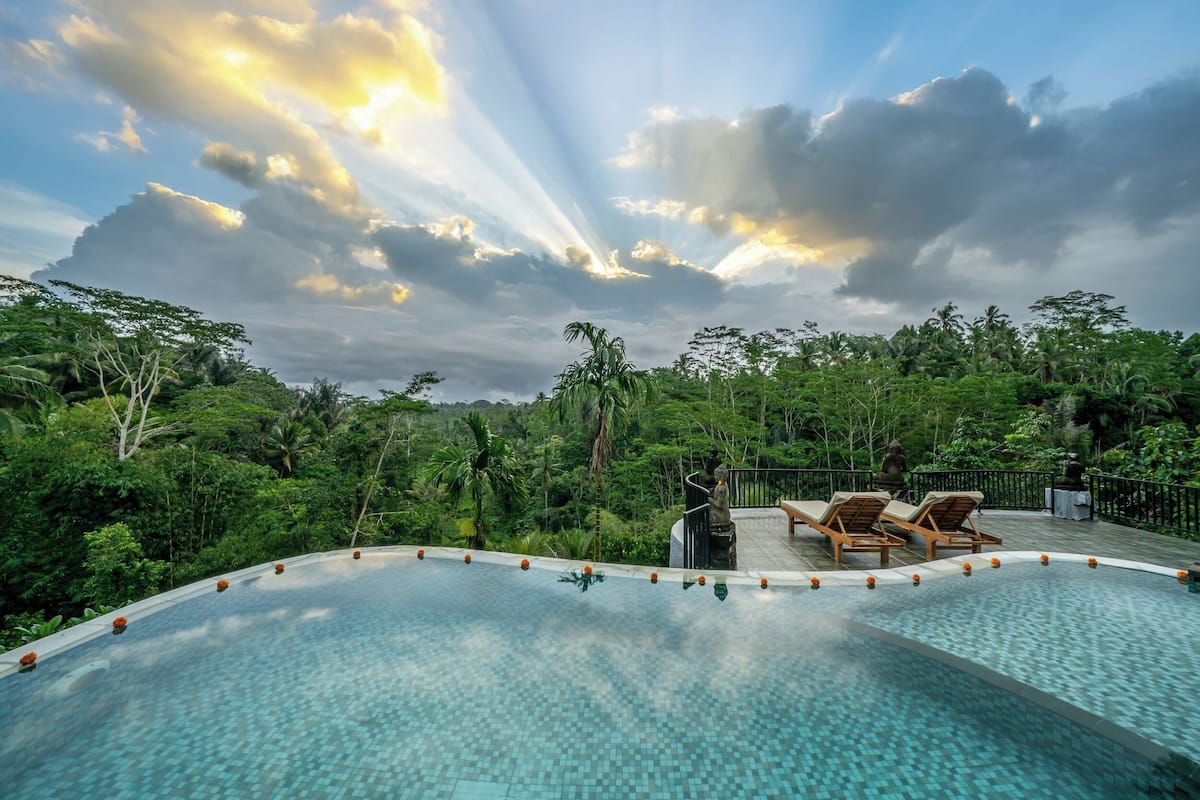 An infinity pool with a view of lush greenery and a cloudy sky.