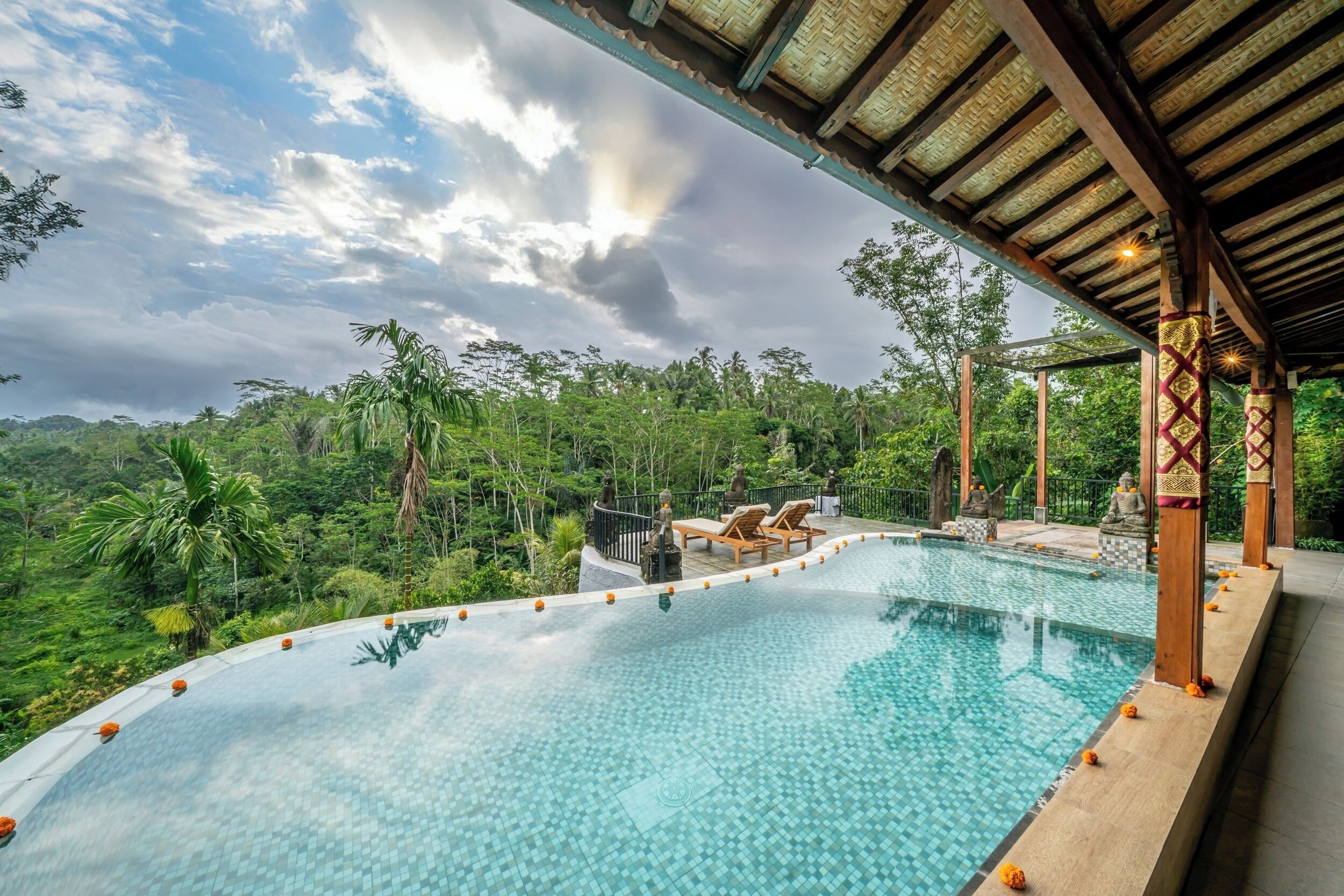 Piscina infinita com vista para vegetação exuberante e céu nublado.